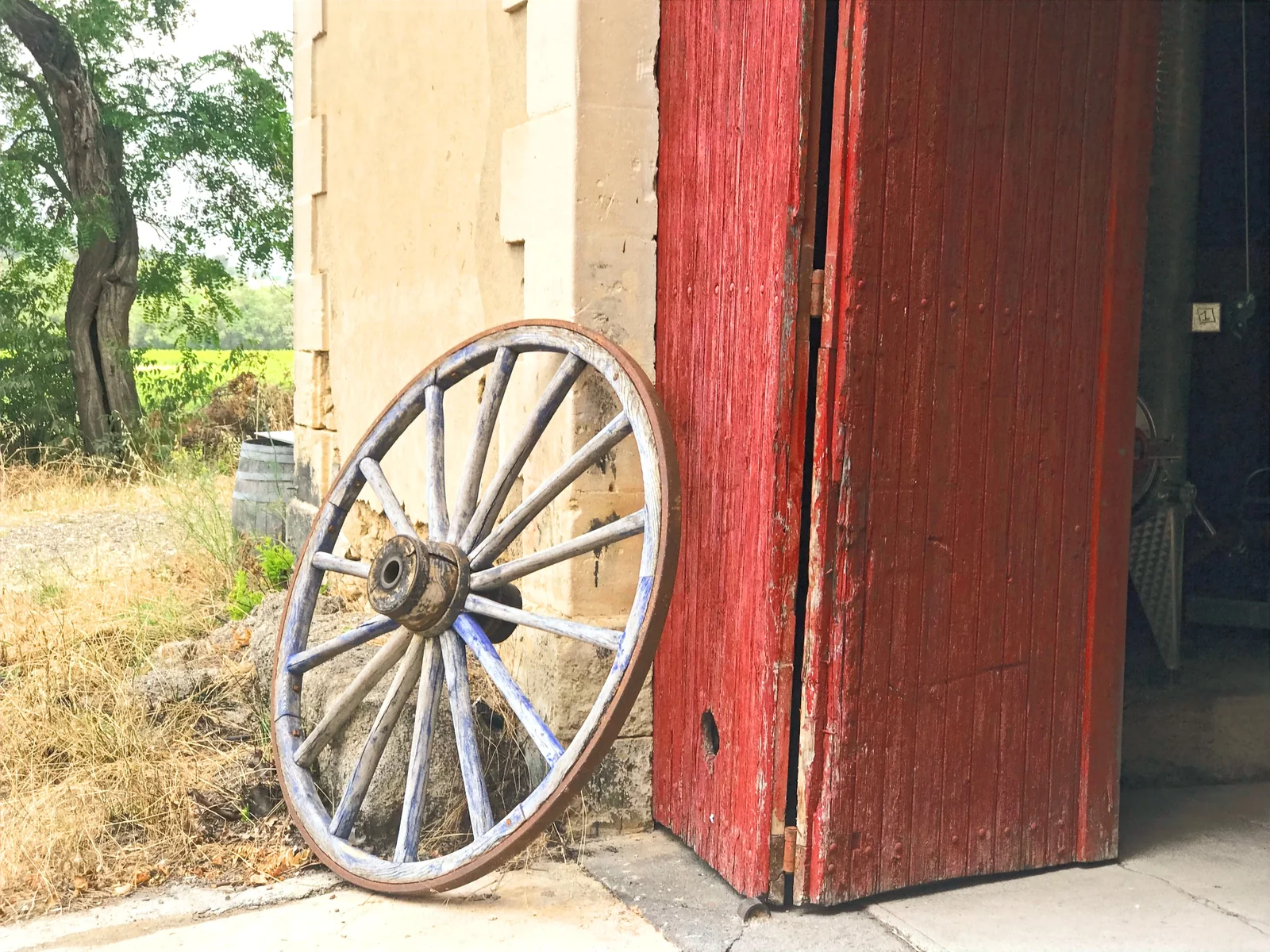 Porte de chai rouge patine et roue de charrette. Cachet rural.